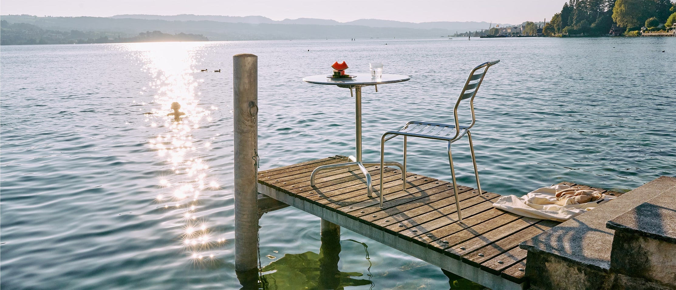 feuerverzinkter Stuhl und Klapptisch auf einem Steg am See bei Sonnenuntergang