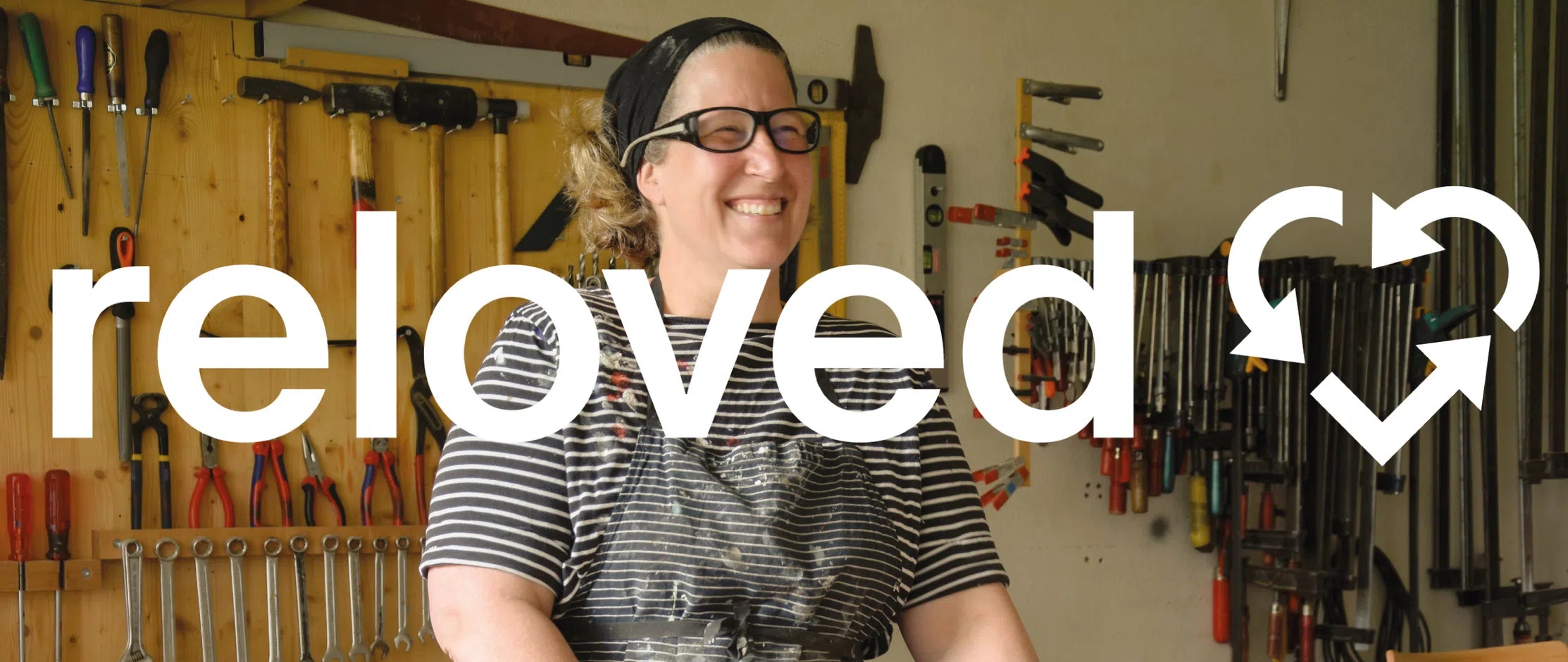 Eine Person steht in einer Werkstatt mit Werkzeugen an der Wand. Der Text "reloved" ist über das Bild gelegt.