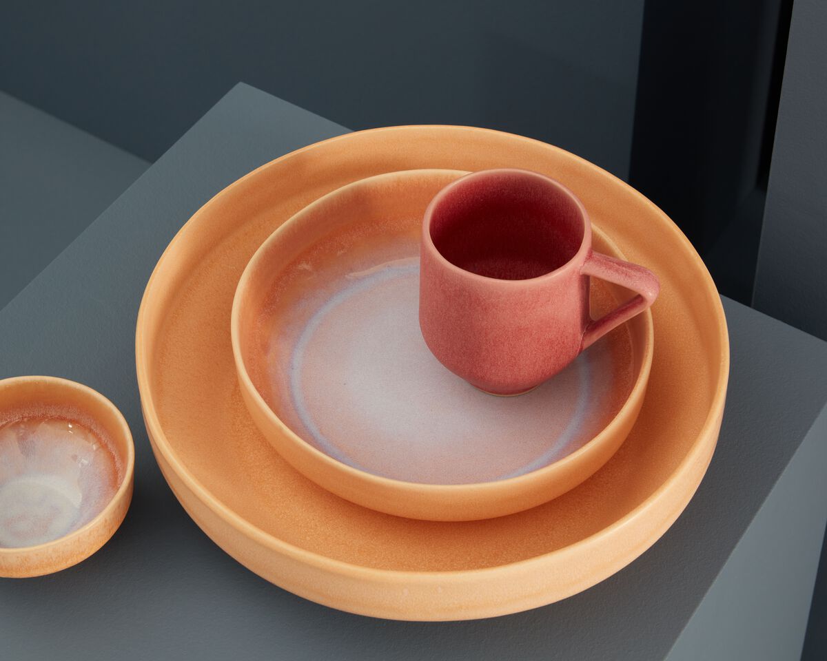 Modernes SPHERE Geschirr-Set in warmen Orange- und Rottönen, bestehend aus Tellern, einer Schale und einer Tasse.