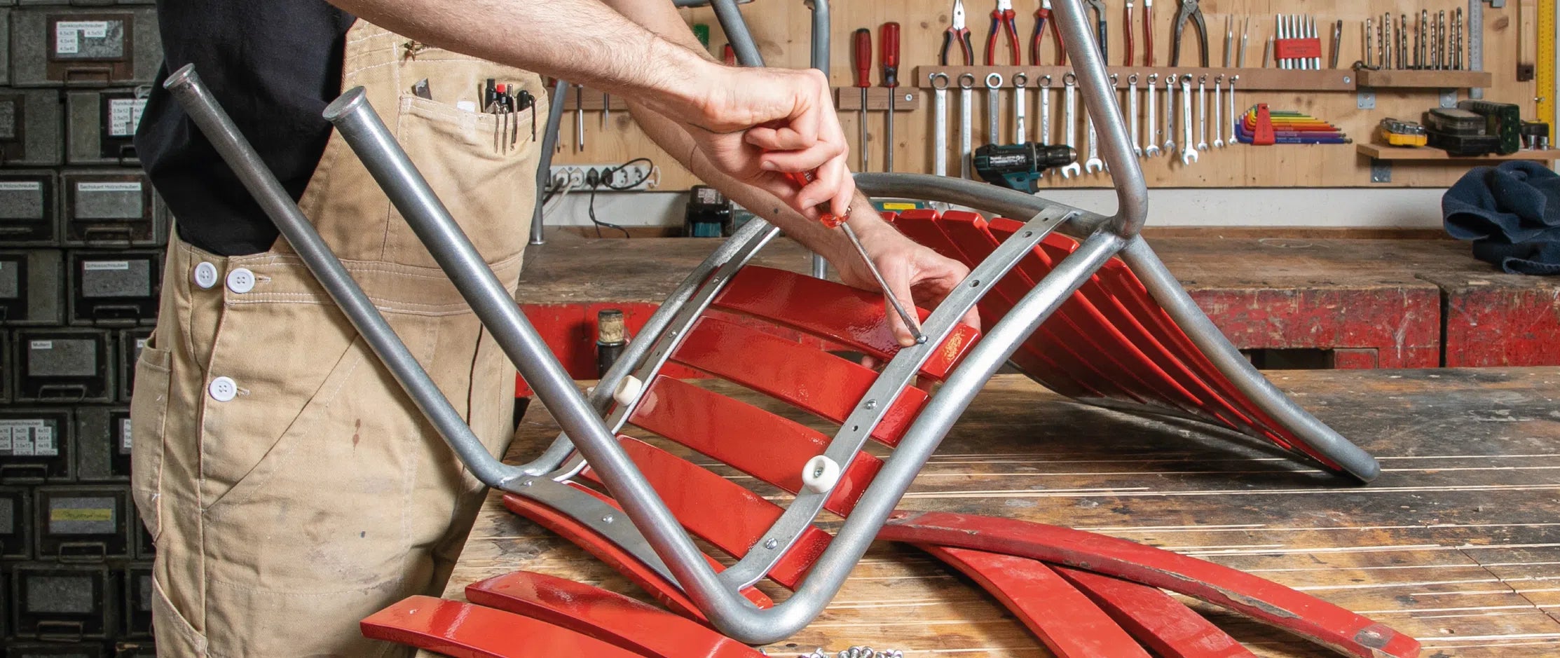 alt="Eine Person repariert einen umgedrehten roten Stuhl in einer Werkstatt."