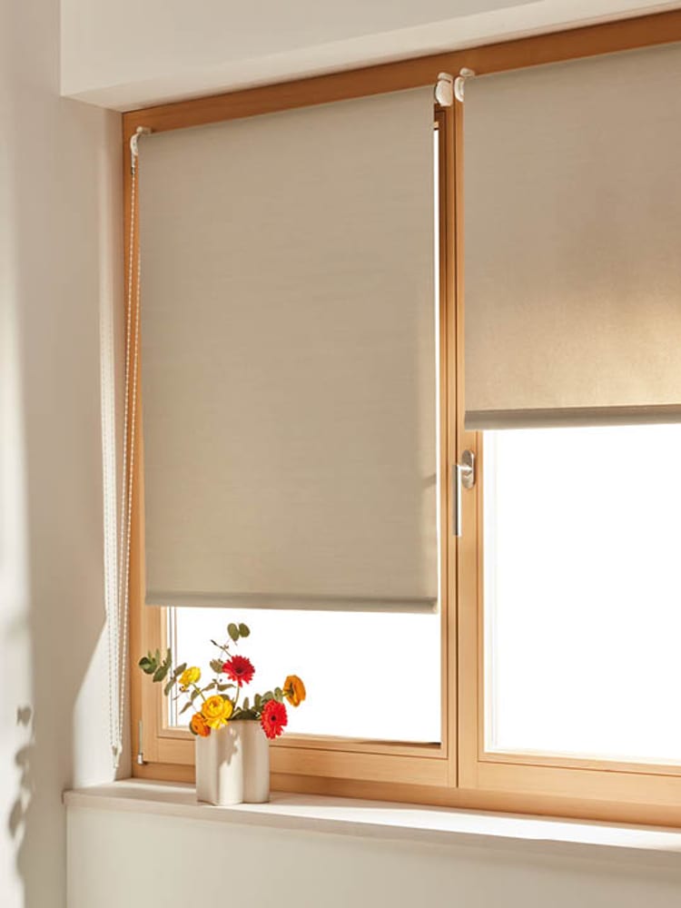 Helle Rollladen-Vorhänge an Holzfenstern mit Blumen auf der Fensterbank.