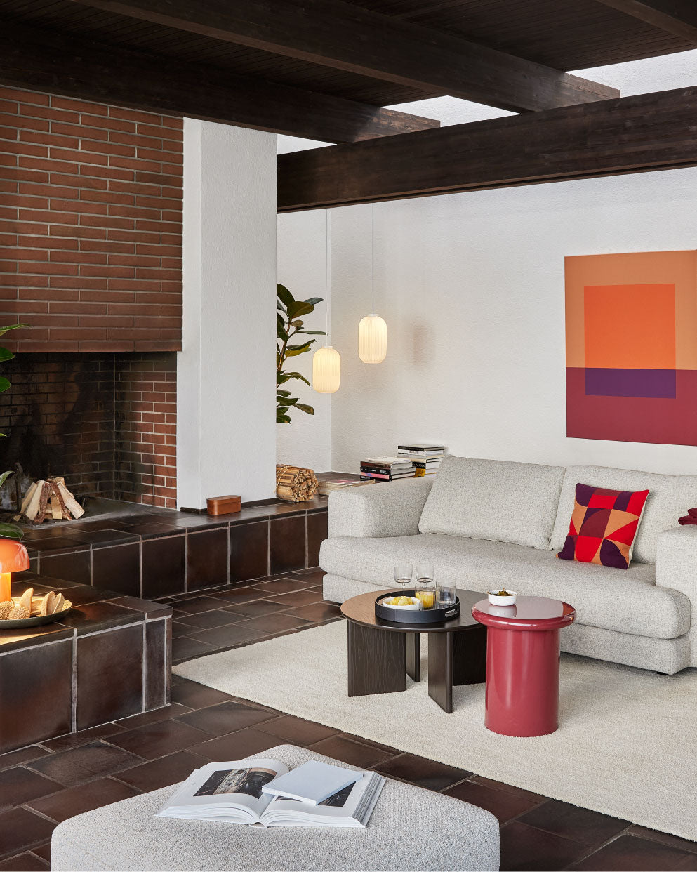 Modernes Wohnzimmer mit hellem Sofa, roten Akzenten, Kamin und zwei runden Couchtischen.