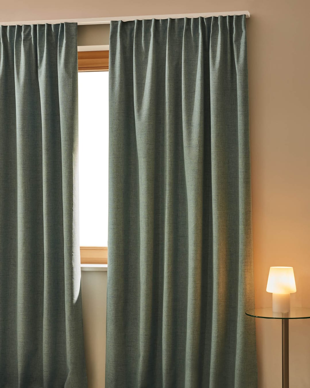 Dunkler Nachtvorhang vor einem Fenster mit Tischlampe daneben.