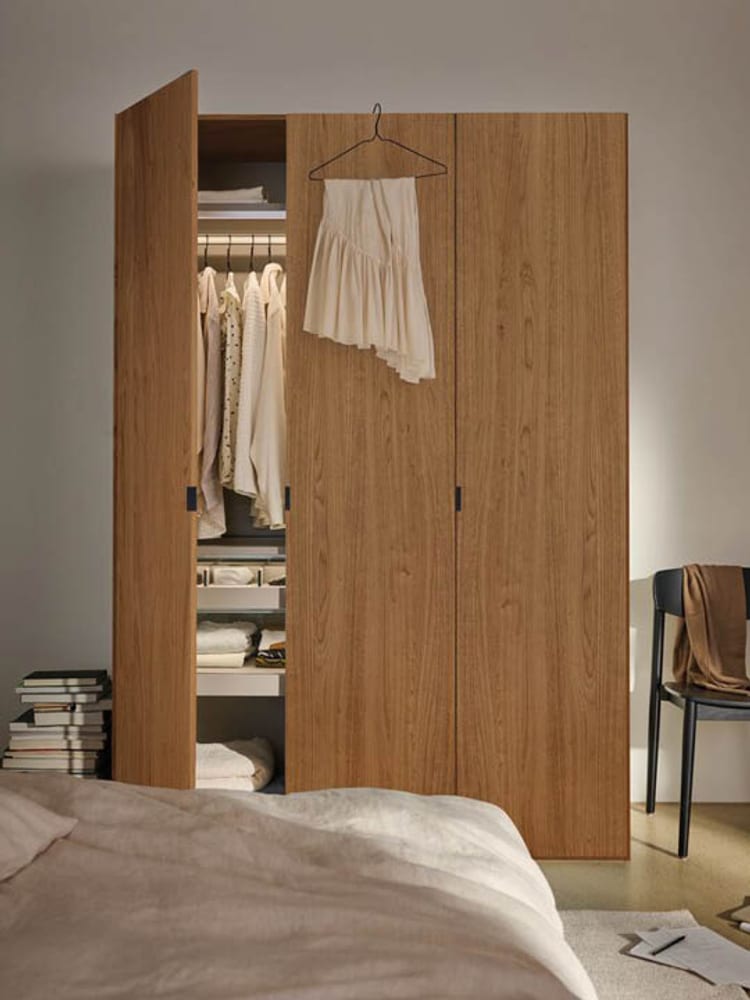 Moderner Kleiderschrank aus Holz mit geöffneter Tür und heller Kleidung.