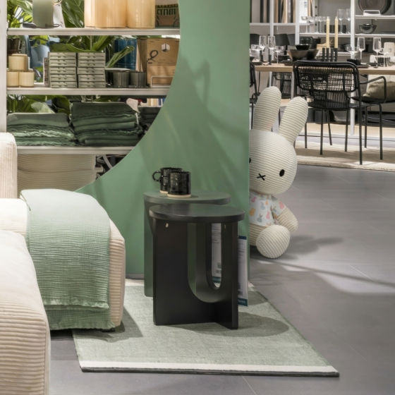 Wohnbereich mit cremefarbenem Sofa, mintgrünen Textilien, schwarzem Beistelltisch und großer Stofffigur in Hasenform im Hintergrund.
