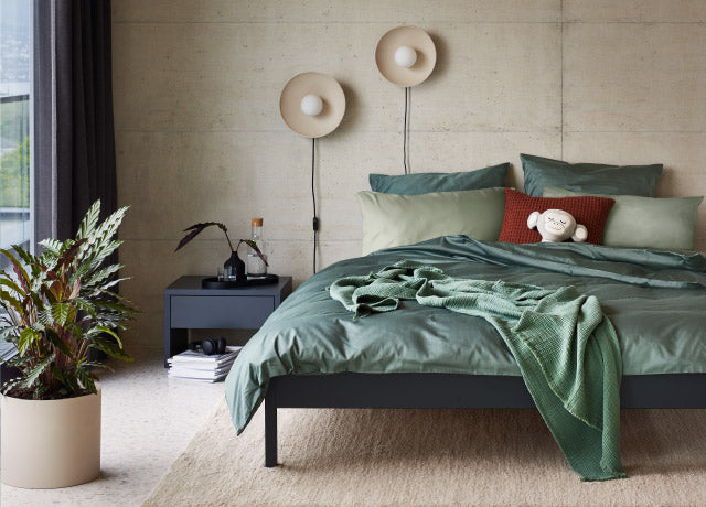Modernes Schlafzimmer mit gruenem Bettzeug, Kissen, Stofftier und Zimmerpflanze