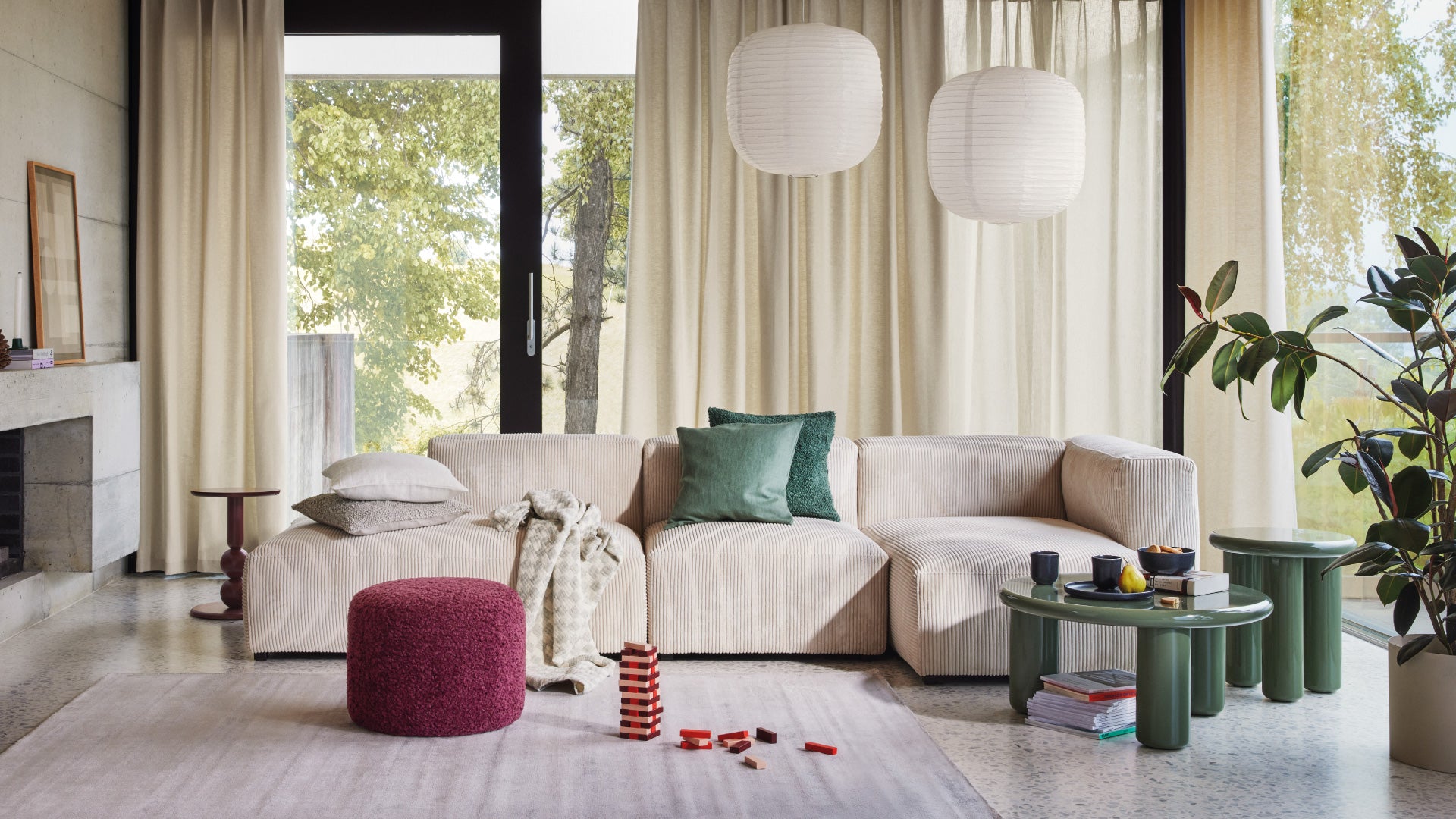 Modernes Wohnzimmer mit beigem Sofa, roten Akzenten und viel Tageslicht durch grosse Fenster.