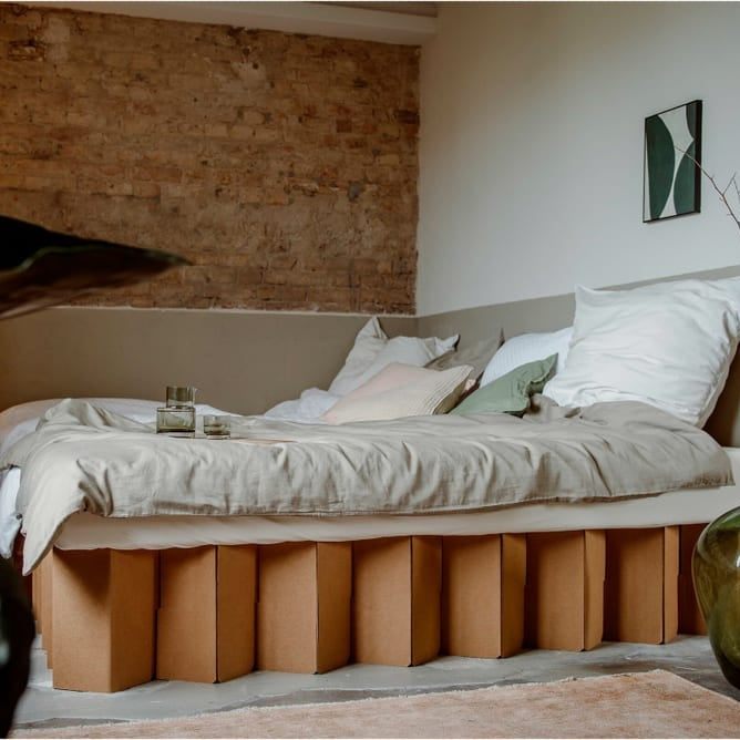 Gemütliches Bett mit nachhaltigem Untergestell aus Karton in einem stilvoll eingerichteten Raum.