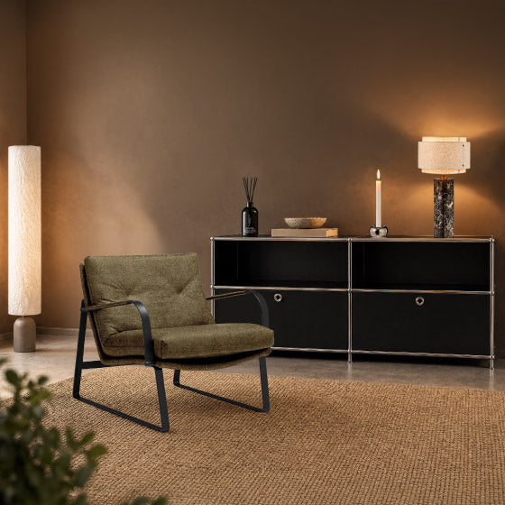 Accogliente poltrona da salotto davanti a una credenza nera, con lampade di design e complementi d'arredo in un ambiente dall'atmosfera calda.