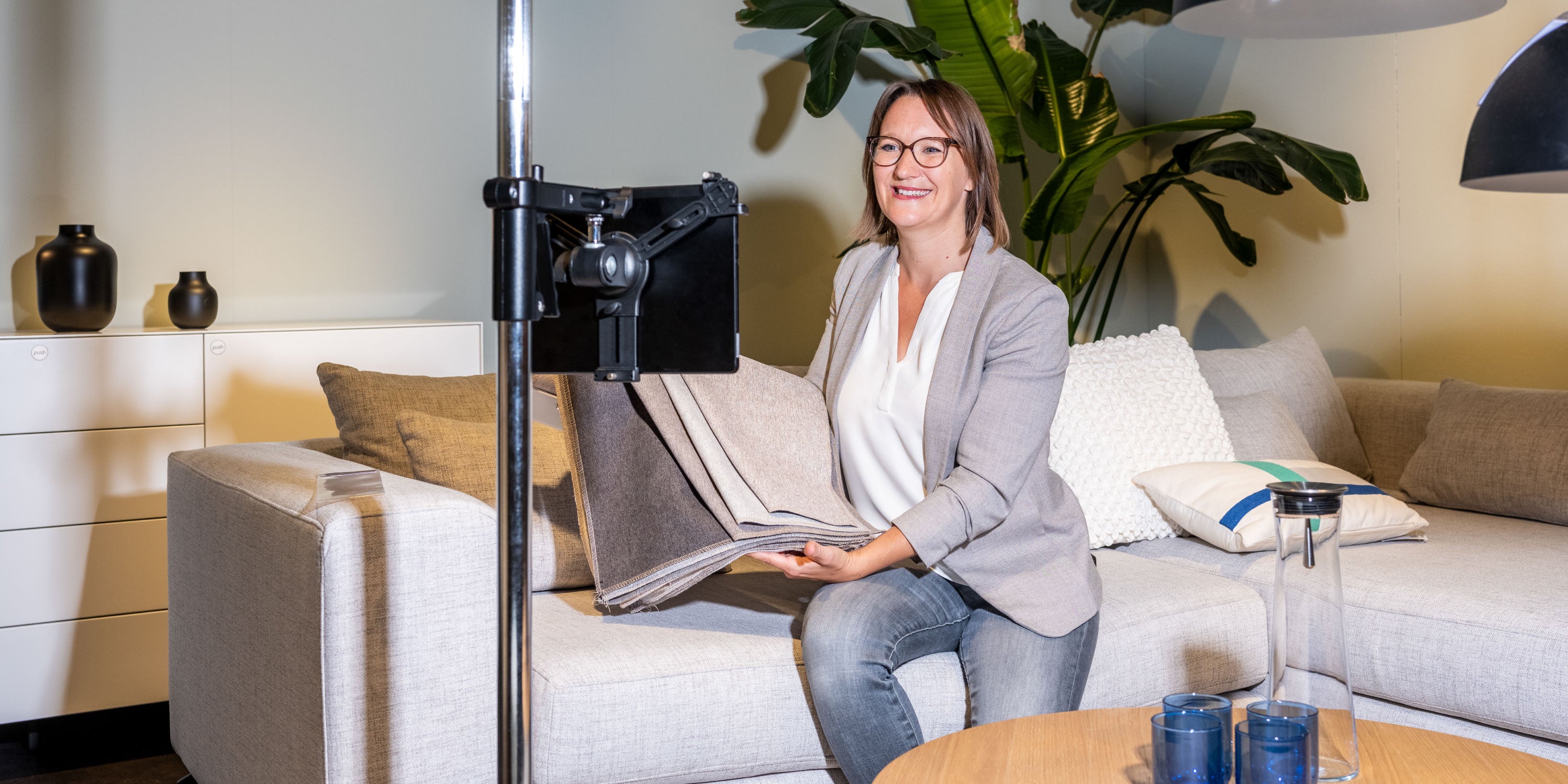 Person sitzt auf einem Sofa und präsentiert Stoffmuster vor einer Kameraeinrichtung.