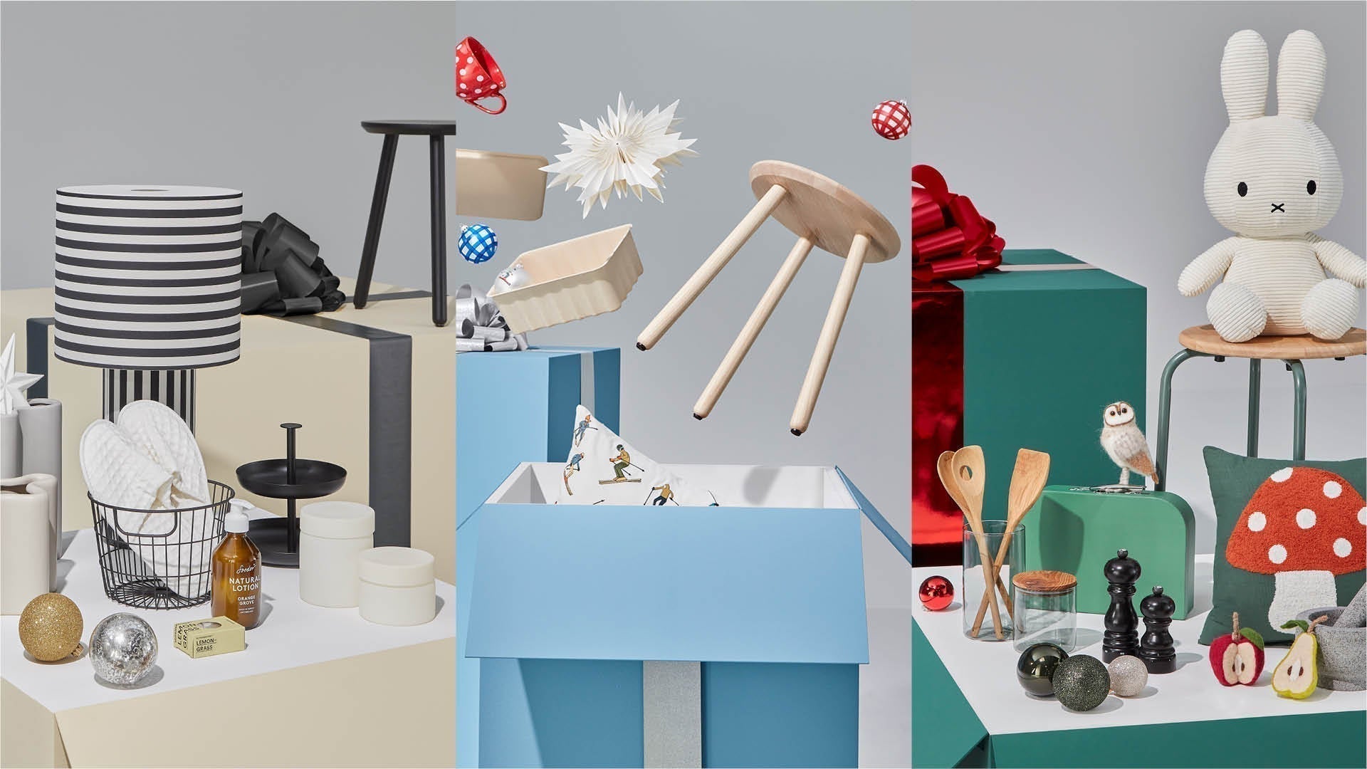 Geschenkideen auf farbigen Boxen: links Lampen, Geschirr und Deko; in der Mitte blaue Geschenkbox mit Hocker und Stern; rechts Stofftier, Küchenutensilien und kleine Dekoobjekte.