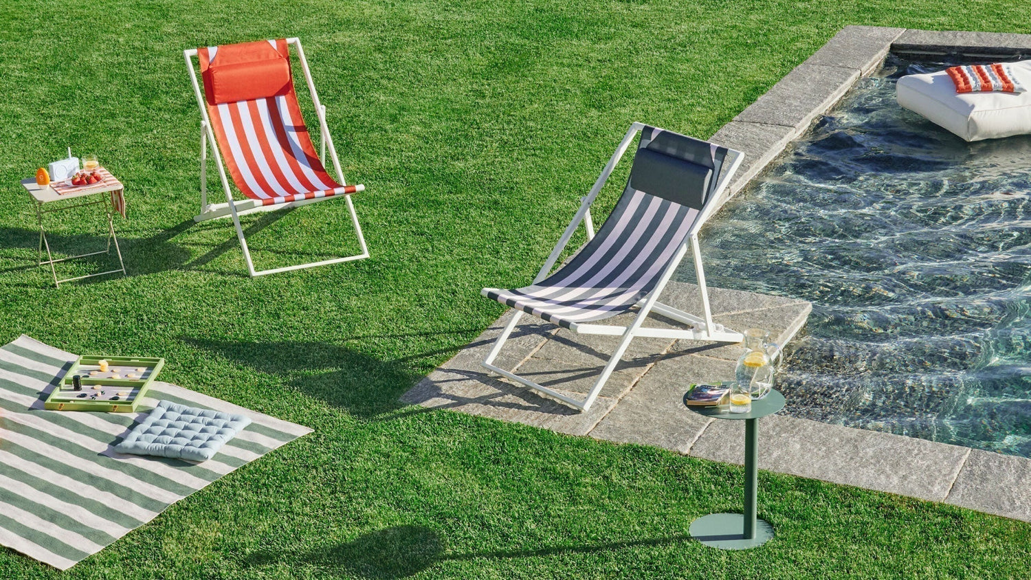Liegestühle und Outdoor-Zubehör auf einer Rasenfläche neben einem Pool an einem sonnigen Tag.