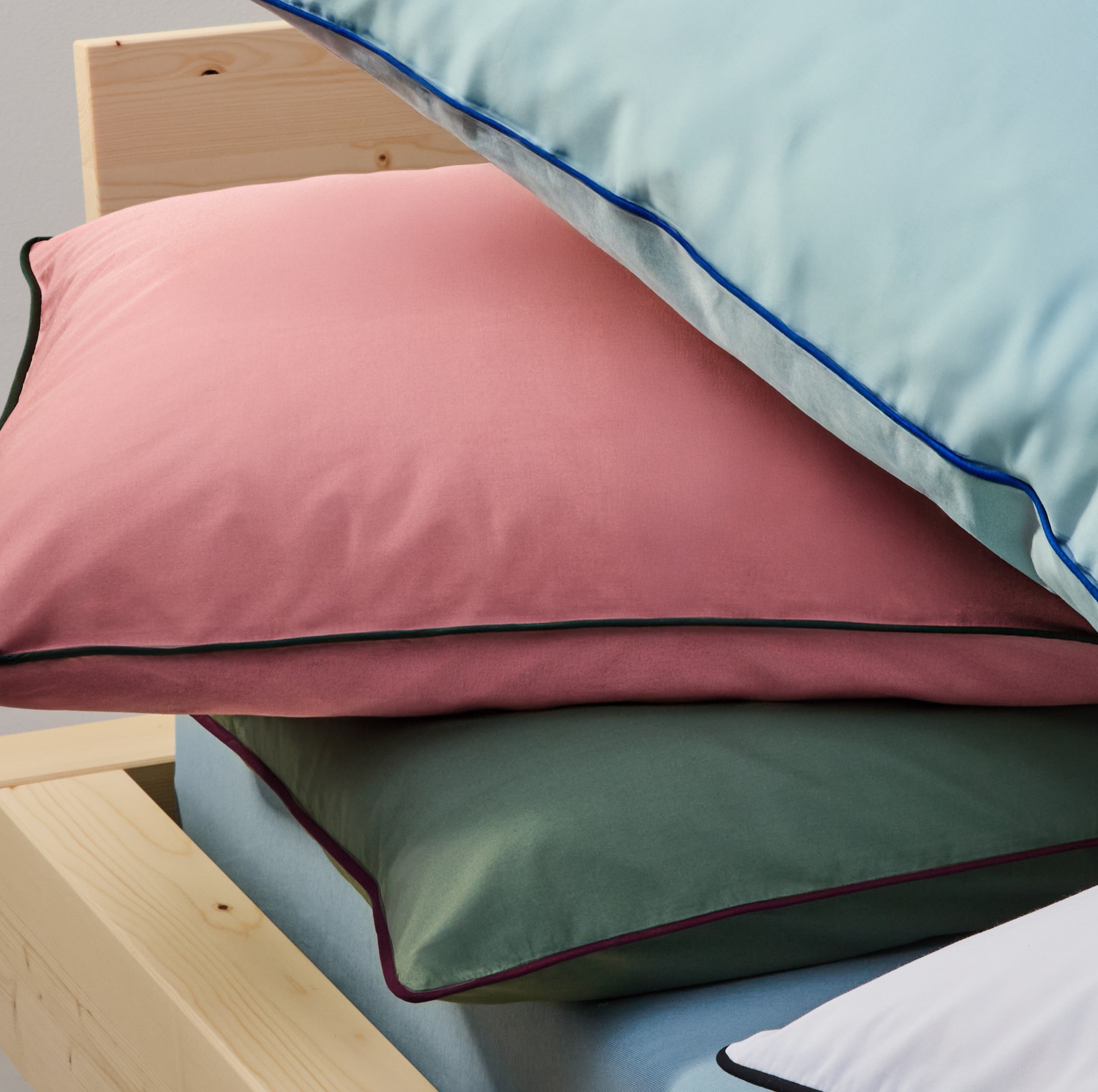 Gestapelte Kissen in Rosé, Grün und Blau auf einem Holzbett.