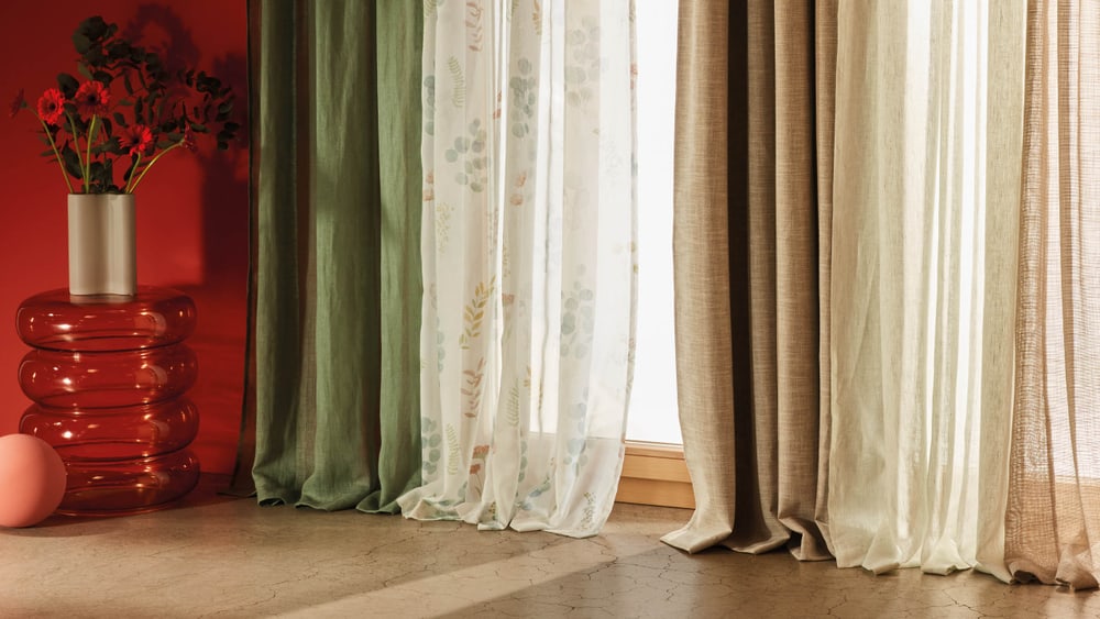Verschiedene Vorhänge in warmen Farben und leichten Stoffen vor einer roten Wand mit dekorativer Vase.