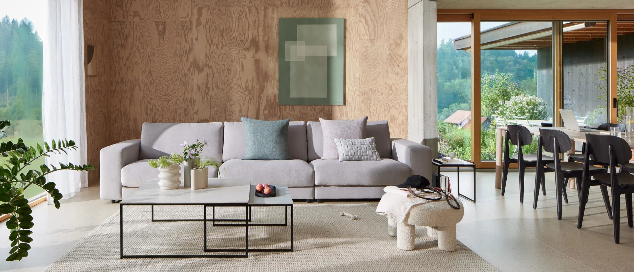 oggiorno elegante con divano moderno e accenti chiari, vista su un giardino verde attraverso grandi finestre.