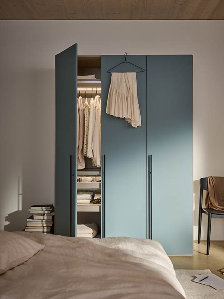 Ein geöffneter blauer Kleiderschrank in einem Schlafzimmer mit Kleidung und Büchern.