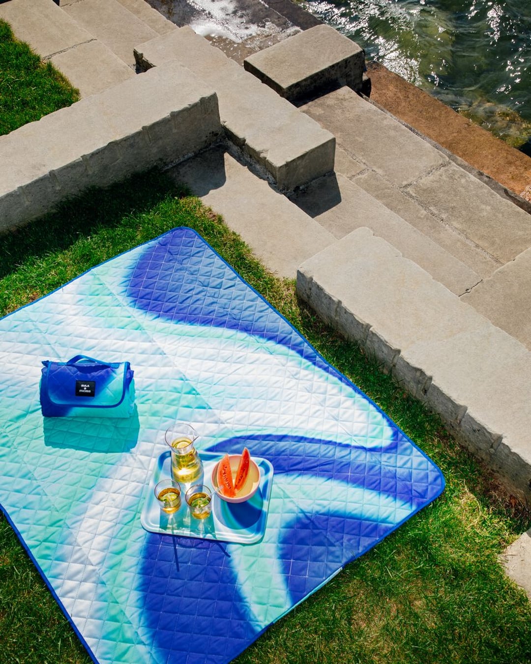 Couverture de pique-nique près de l&apos;eau avec boissons et pastèque sur un plateau.
