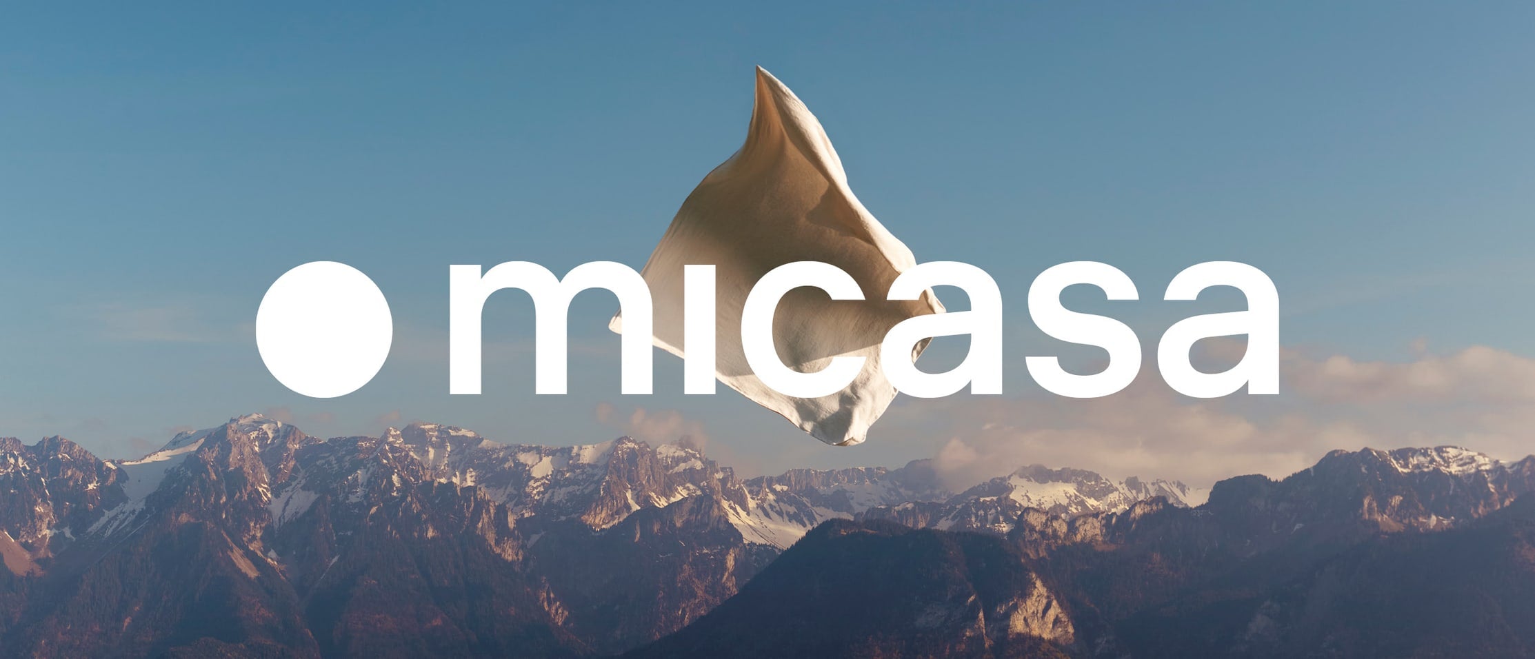 Logo Micasa davanti a un paesaggio montano con biancheria da letto fluttuante.