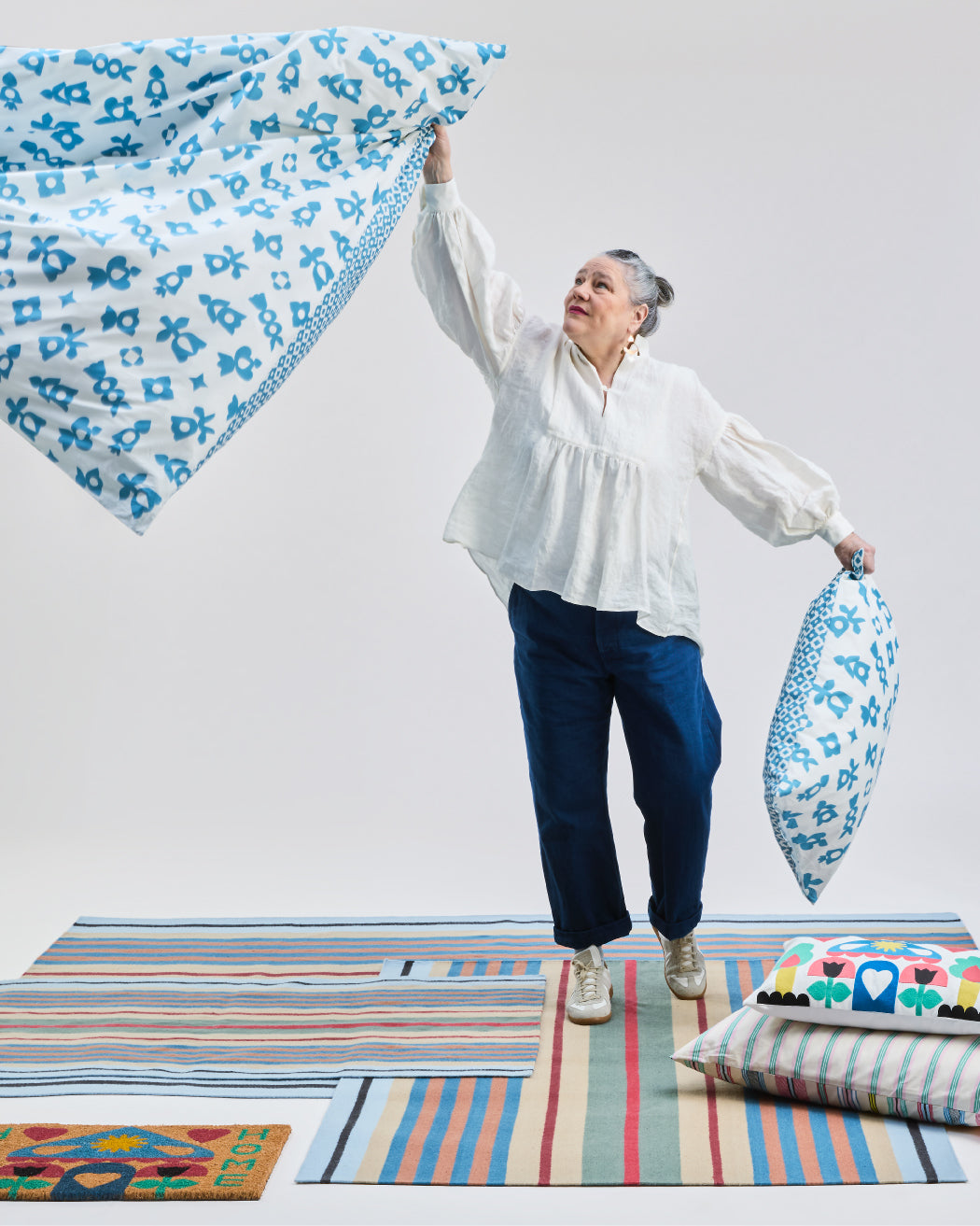 Person mit gemusterten Textilien und Kissen auf farbigen Teppichen.