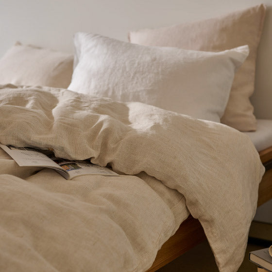 Helle Leinenbettwäsche in Beige mit weissen Kissen auf einem Bett.