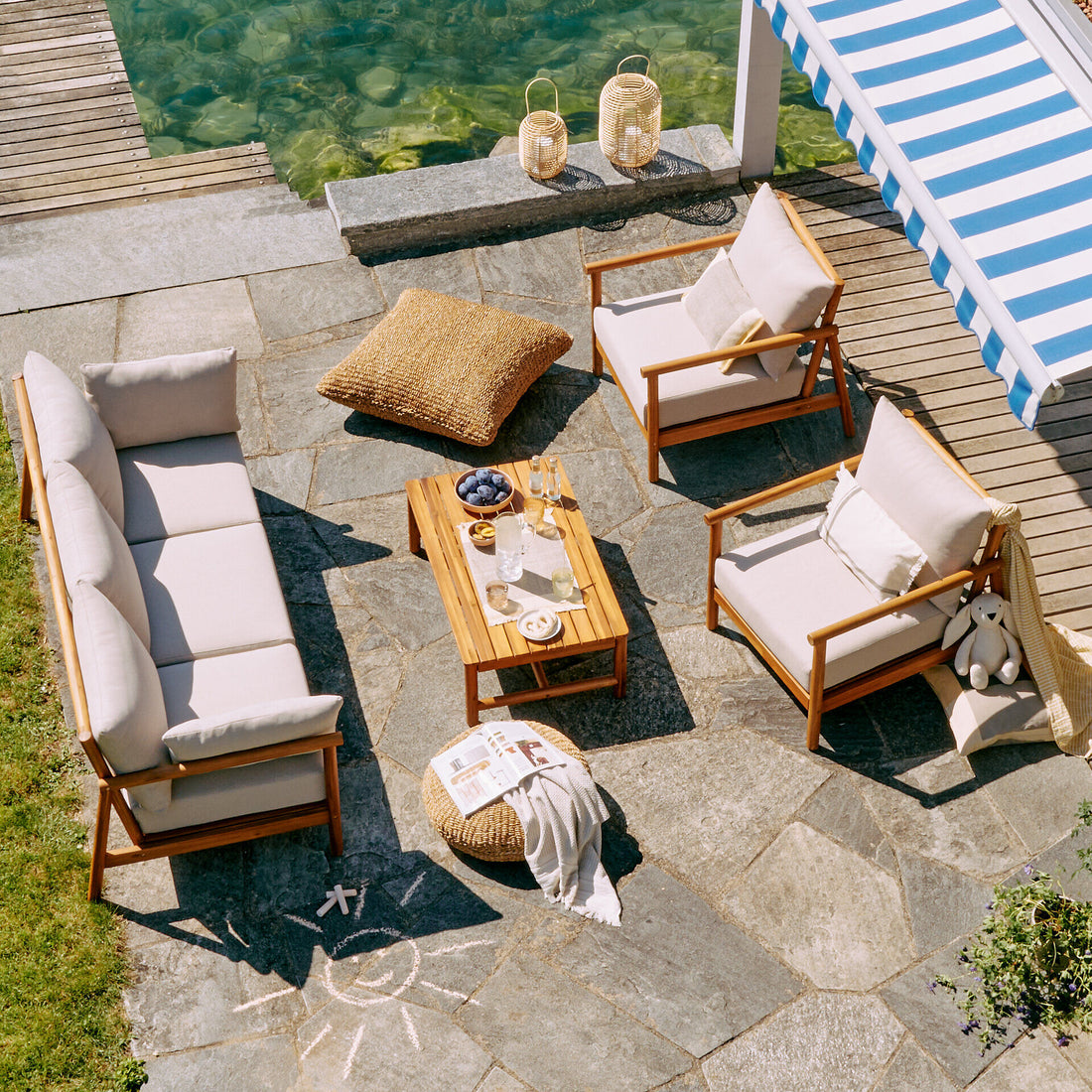 Outdoor-Lounge mit Holzsofa, Sesseln und Couchtisch auf einer Steinterrasse neben einem Pool unter einer gestreiften Markise.