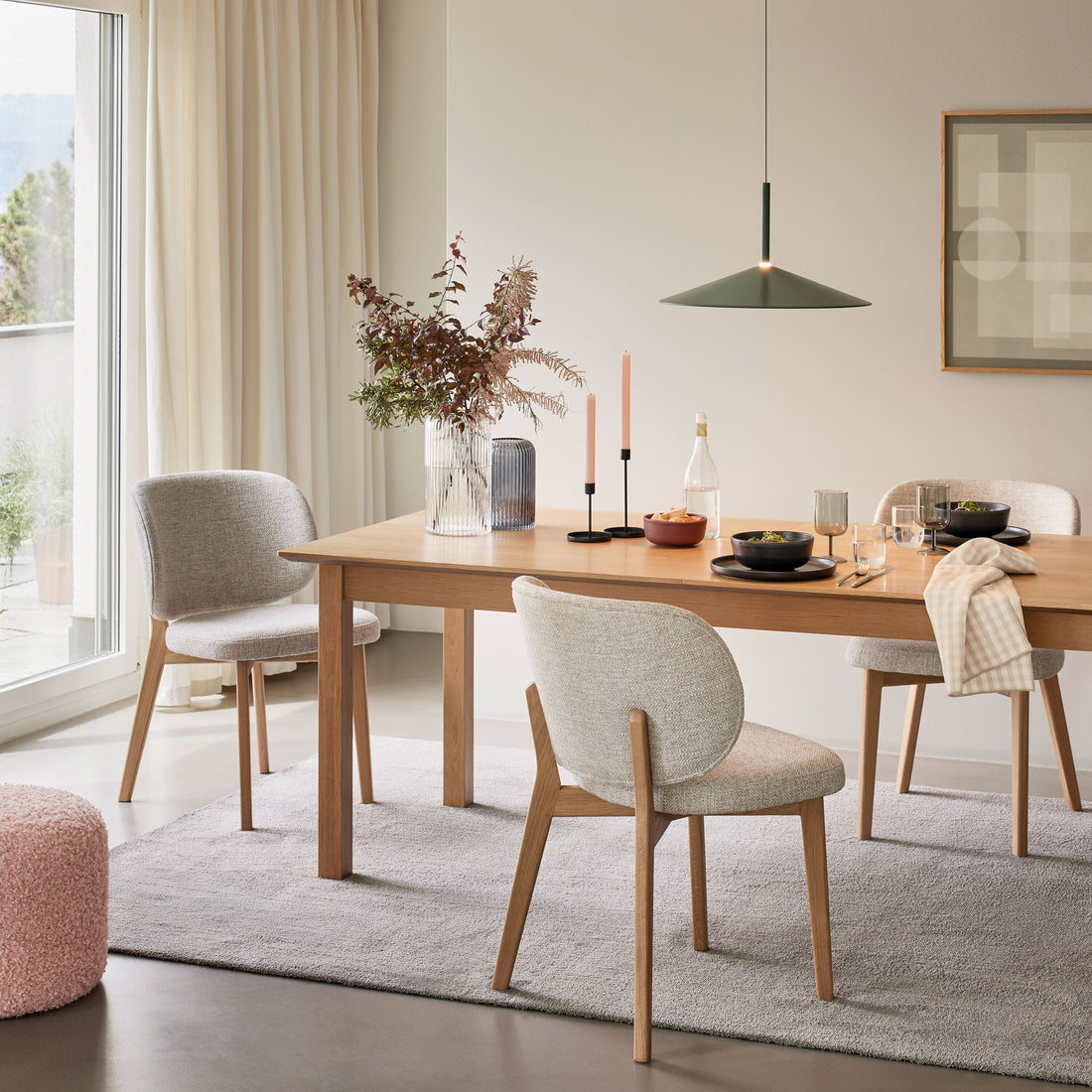 Modern eingerichtetes Esszimmer mit Holztisch, hellen Polsterstühlen, dekoriertem Gedeck und großen Fenstern mit Vorhängen.