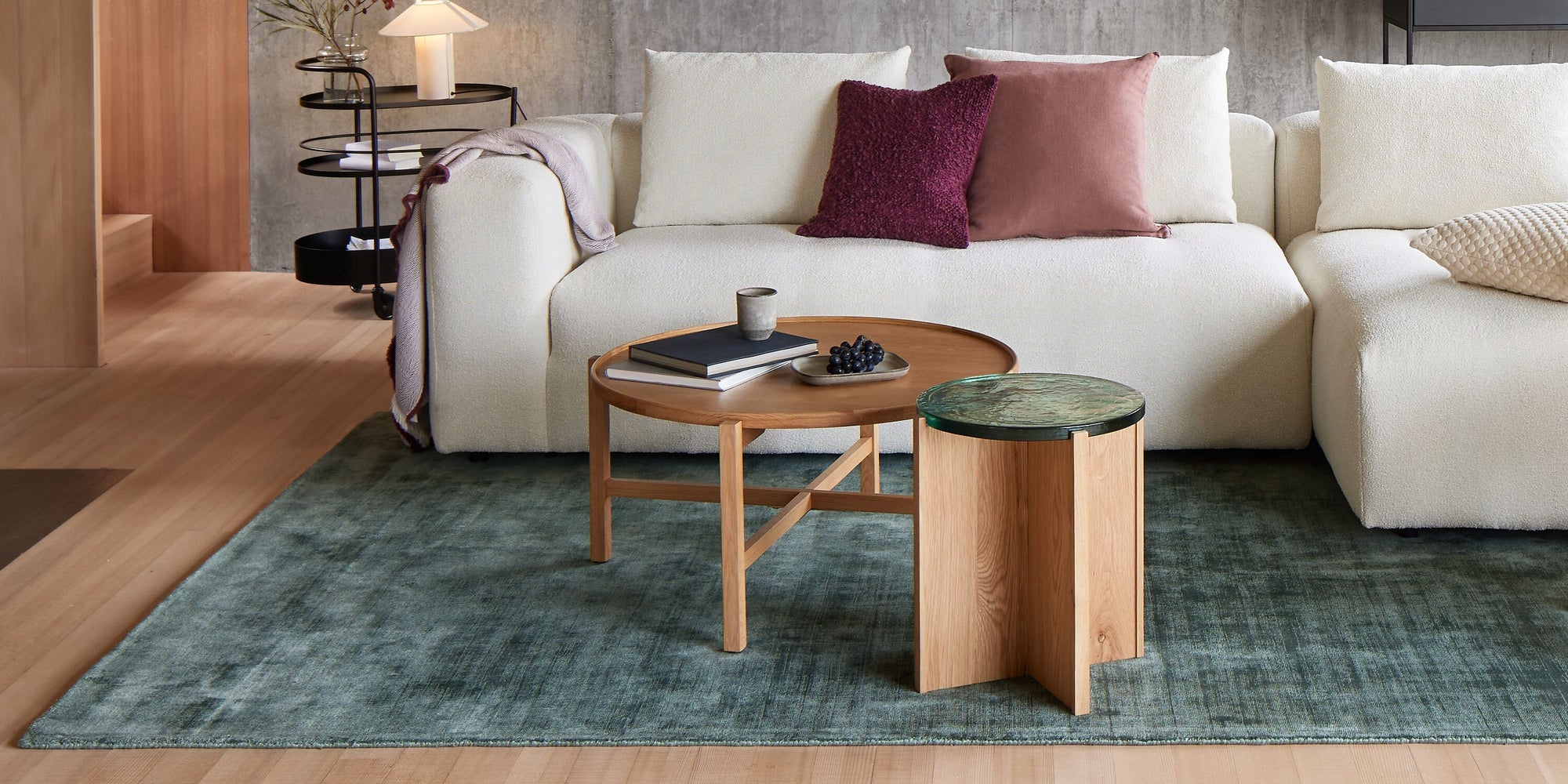 Wohnzimmer mit cremefarbenem Bouclé-Ecksofa, Holz-Couchtischen und grünem Teppich in modernem Ambiente.