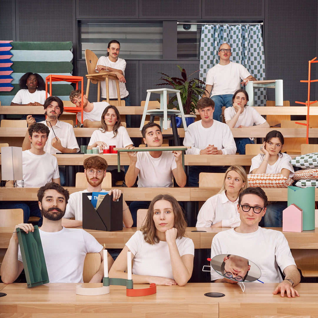 Gruppe von Personen in weisser Kleidung in einem minimalistisch eingerichteten Raum mit Betonwand, Pflanzen, Möbeln und Dekorationen.
