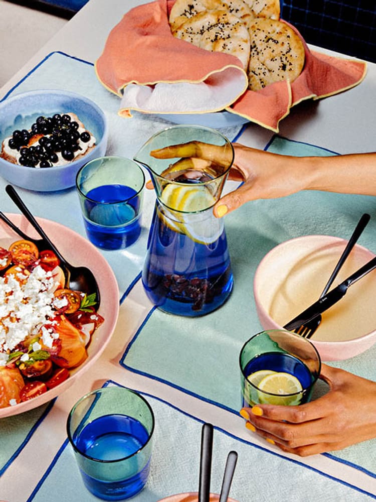 Table avec des assiettes colorées, une salade, du pain et une carafe d&apos;eau avec des baies.