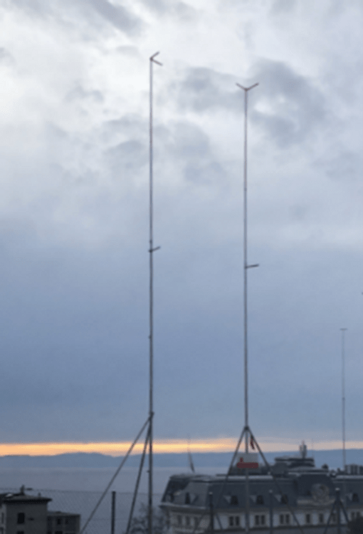 Deux grandes antennes devant un ciel nuageux avec vue sur des toits et un lac en arrière-plan.