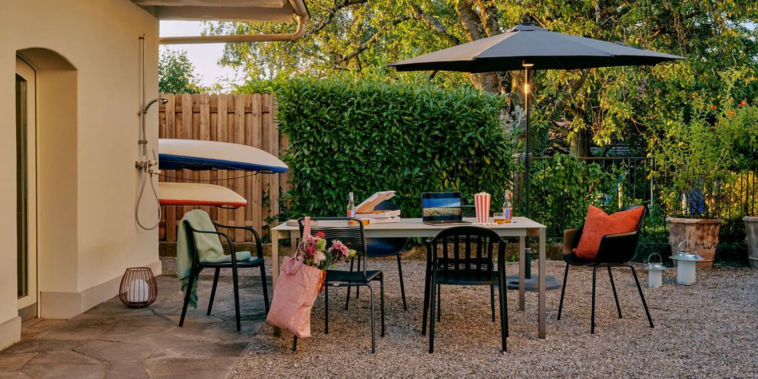 Eine gemuetliche Terrasse mit Tisch, Stuehlen, Sonnenschirm und Kajaks an der Wand.