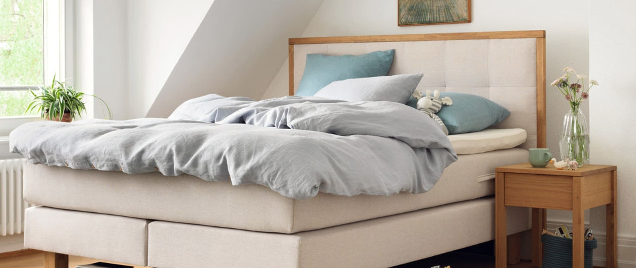 Boxspringbett auf einem Parkettboden und Bücher auf dem Boden.