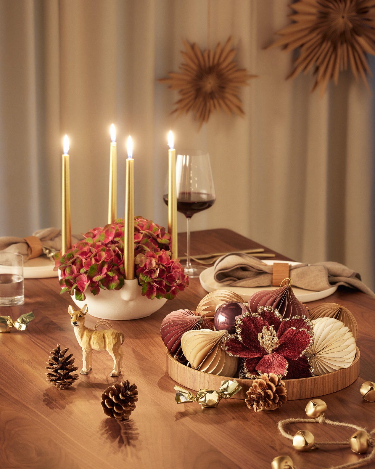 Festlich gedeckter Tisch mit goldenen Kerzen, Blumenarrangement, Weihnachtsdekoration, Tannenzapfen und einem kleinen Hirschfigur.