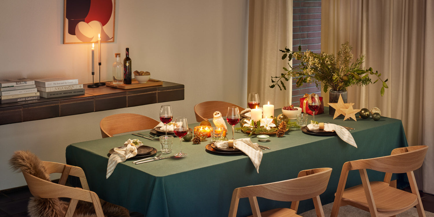 Festlich gedeckter Tisch mit grüner Tischdecke, Kerzen, Wein, Tannenzweigen und Weihnachtsdekoration.