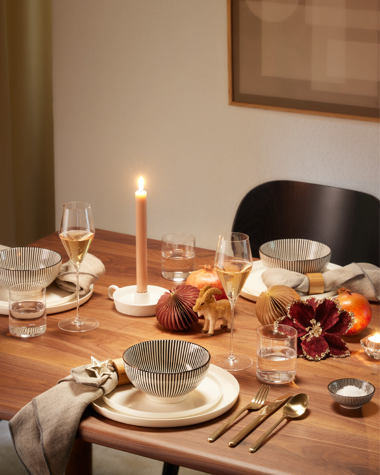 Festlich gedeckter Tisch mit Kerze, Geschirr, Gläsern und Weihnachtsdekoration in warmen Farben.