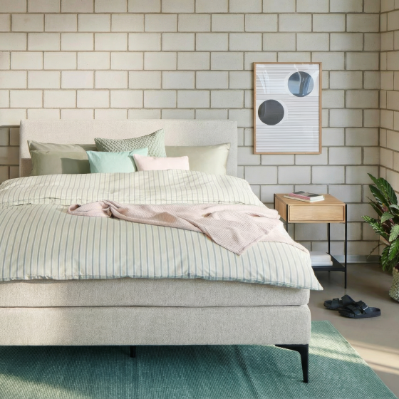 Modern eingerichtetes Schlafzimmer mit gepolstertem Bett, Nachttisch und pastellfarbener Bettwäsche.