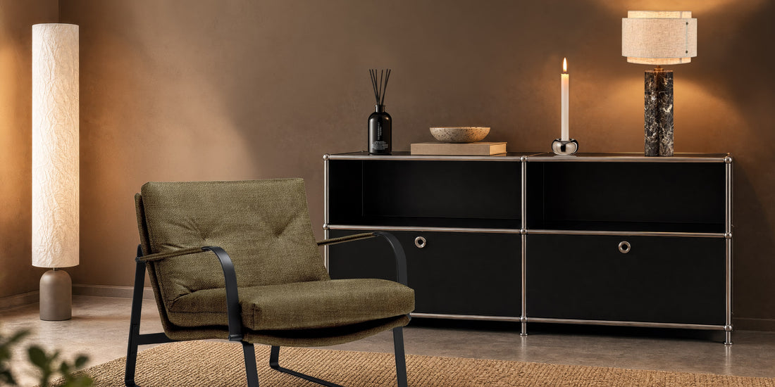 Gemütlicher Loungesessel vor schwarzem Sideboard mit stilvollen Leuchten und Wohnaccessoires in warmem Ambiente.
