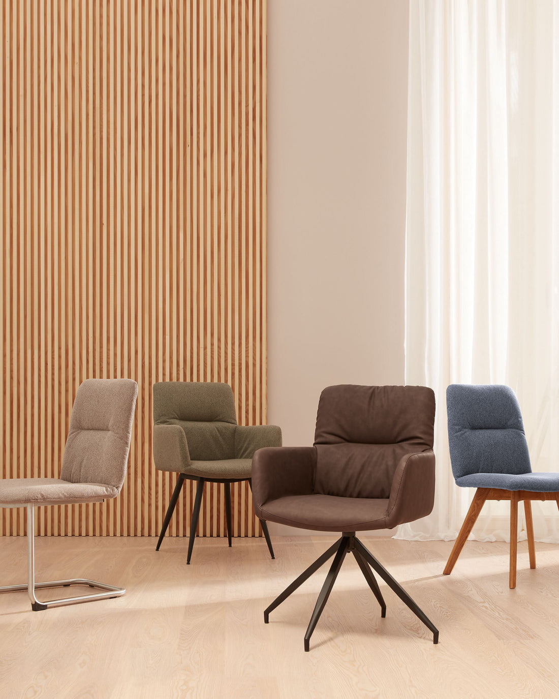 Mehrere moderne NAVIGLI Polsterstühle in unterschiedlichen Farben stehen in einem hellen Raum mit Holzlamellen-Wand und bodenlangen weißen Vorhängen.