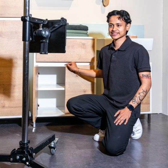 Person kniet vor einem Badmöbel und zeigt dessen geöffnete Schranktüren vor einer Kameraeinrichtung.